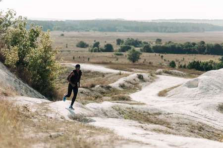 African American fitness men, in sportswear, running along the rocky path on the mountain, muscular...