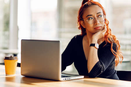 Smiling asian college student wearing glasses sits at a table working online with a laptop, She uses a laptop and studies onlineの写真素材