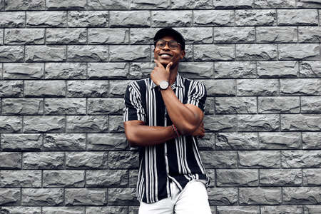 African American man in a shirt in a line, against the background of a black brick wall, stylish guy, with folded hands, posing at the cameraの写真素材