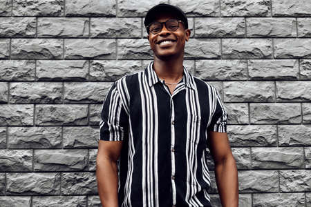 African American man in a shirt in a line, against the background of a black brick wall, stylish guy posing in front of the camera, wearing glasses, dark-skinned guy modelの写真素材
