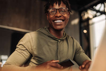African American man with a laptop and a phone in his hands, sitting at a table in the office. work...