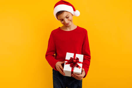 handsome young boy in a red sweatshirt with a gift and a santa claus hat. holding a Christmas present. christmas concept, new year, lovers day.の写真素材
