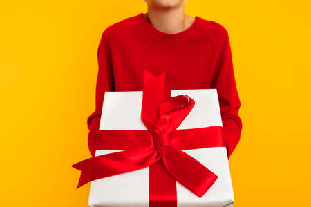 close-up of a gift in the hand of a little boy. on a yellow background. christmas concept, new year, lovers day. on Christmas Eve. white gift with a red bowの写真素材
