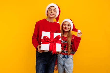 Christmas two friends, a boy and a girl in santa claus hats and gifts, on a yellow background. christmas eve and new year. selection of gifts for the holiday.の写真素材