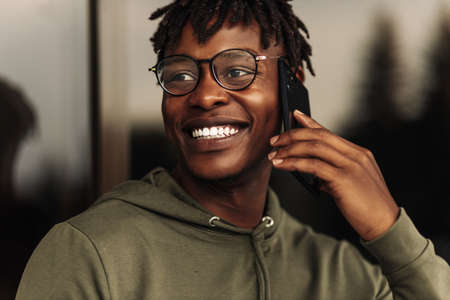Smiling african american man, wearing glasses, with afro hairstyle, professional business call, talking on the phone outdoors in the street, enjoying corporate mobile conversation, close-up side viewの写真素材