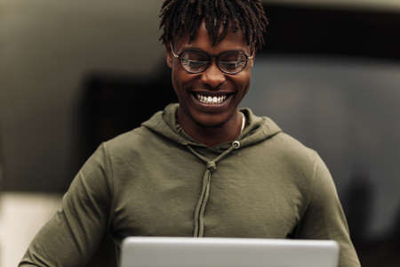 Focused african american college student, wearing glasses working on laptop sitting on stairs in campus preparing for examの写真素材