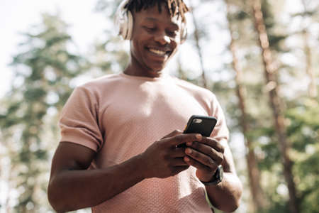 Portrait of African American athletic man listening to music with wireless headphones and using...