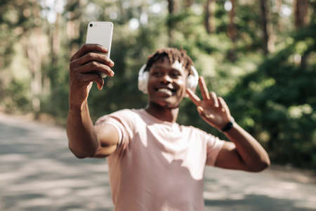 Self portrait of handsome sporty african american man, taking selfie on mobile phone, taking peace sign, outdoors, selfie conceptの写真素材