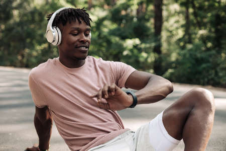 Attractive sporty African American man, dressed in sportswear, listening to music with headphones...