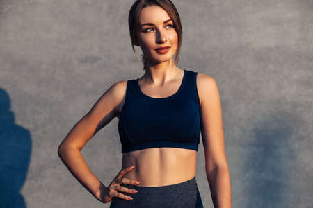 Portrait of a beautiful smiling healthy fitness woman, with a beautiful athletic body, in sportswear, happy woman after fitness, against the background of a gray city wall, concept, sport, motivationの写真素材