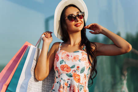 Fashionable beautiful happy woman, in a dress and black glasses, look in a shop window, standing with shopping bags near a shopping center on Black Fridayの写真素材