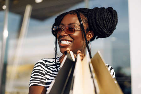 Black Friday Sale, Attractive young American woman holding shopping bags and smiling while standing outdoors near shopping mallの写真素材