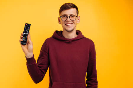 Man in glasses with remote control gradually changing over isolated yellow background. cheerful man...