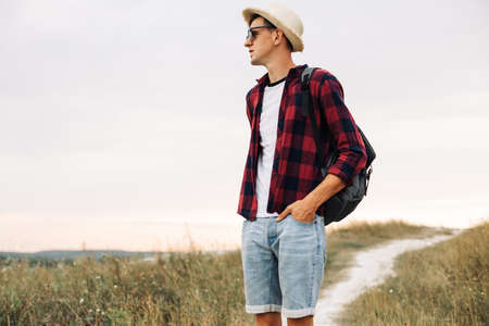 Hiker with a backpack, sunglasses and a hat, enjoying the view of the valley from the top of the mountain. Happy tourist man walks through the valley. Travel and adventure conceptの写真素材