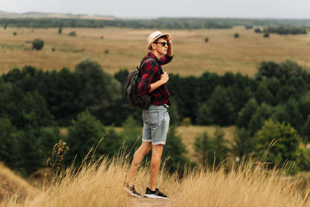 man with a backpack on a country walk on a summer day. Young people hiking in the countryside, outdoors at sunset, traveler wearing hat and sunglassesの写真素材