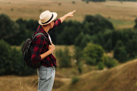 man with a backpack on a country walk on a summer day. Young people hiking in the countryside, outdoors at sunset, traveler wearing hat and sunglassesの写真素材