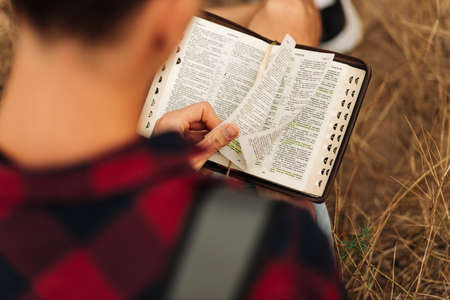 Reading the Bible outdoors in nature. A man in sunglasses and a shlap holds a Bible in his hands, standing in the forest. Faith, spirituality and religion conceptの写真素材