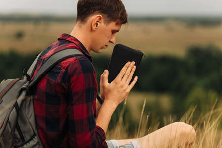 man closed his eyes, prayed in the open air, holding the Bible in his hands. holding a Bible in his hands, standing in nature. Hands folded in prayer of faithの写真素材