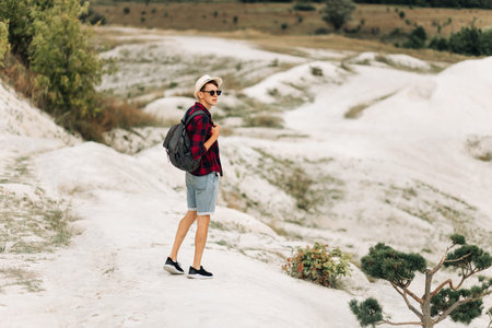 Wanderer with a backpack on the top of the mountains. traveler in a hat and sunglasses. Tourist with...