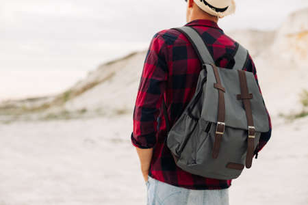 Male hipster traveler with backpack in hat looking forward to amazing mountains and valleys view....
