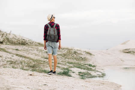 Adventure in the mountains. Young man with a backpack walking along the sandy rocky mountains....