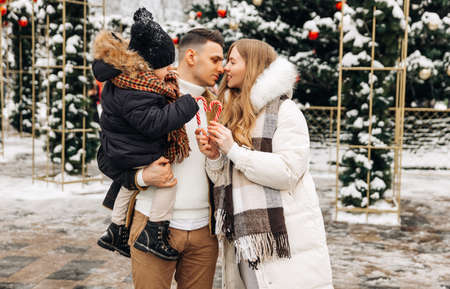loving family mom, dad and child , spending winter holidays together in the city center near the Christmas tree, parents and children having fun near the Christmas stands decoratedの写真素材
