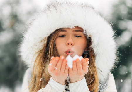 Christmas happy woman in warm winter clothes, street portrait. Winter woman blowing snow in the...