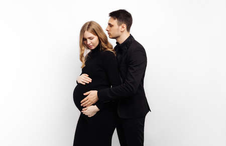 man stands behind his pregnant wife and smiles, hugging her on a white isolated background.Portrait...