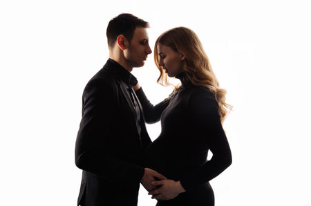 Beautiful pregnancy of a young family. Pregnant woman and man on a white background. Happy couple, wife and husband hugging their tummyの写真素材