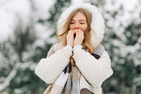 Happy girl warming up her hands in warm winter clothes. Attractive model portrait outdoors on a cold day. Freezing a woman outsideの写真素材