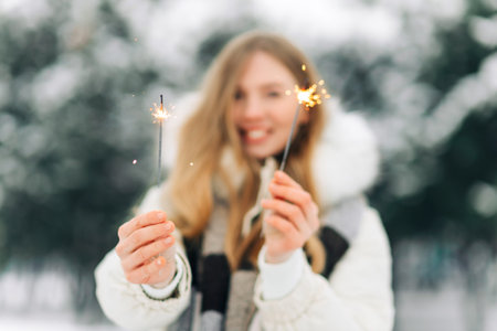 Charming woman in warm winter clothes posing with sparklers on the street in winter. Gorgeous woman...