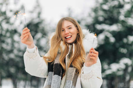 Holidays and celebration concept. Close-up of excited woman with sparklers in hands, outdoors in winter snowy weather, looking at camera happyの写真素材
