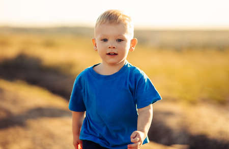Happy little child boy running on the summer meadow in nature. Smiling baby in nature at sunsetの写真素材