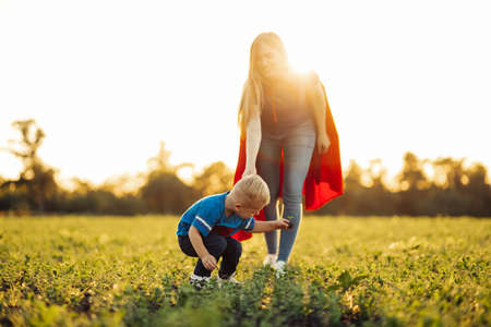 Happy family, Mom and her little son in superhero costumes, plant a tree seedling outdoors on a sunny day. Spring concept, nature and care.の写真素材