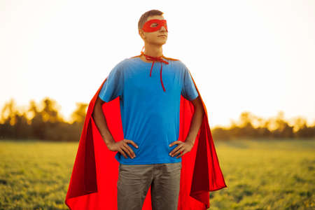 Happy man in a red cape of a super hero and a mask on his face, Strong confident man against the...