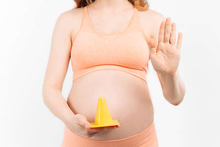 Pregnant woman and expecting a baby over isolated white background, holding her hands on her stomach and showing a prohibition sign. Warning expression with negative and serious gestureの写真素材
