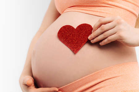 pregnant woman holds a symbol in the shape of a heart in her palms. loving mother is expecting a...