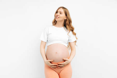 Pregnant happy beautiful woman touches her belly. Pregnant mom caressing her belly and smiling close up. Healthy pregnancy concept, pregnant woman on isolated white backgroundの写真素材