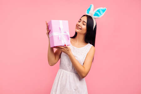 Happy woman in rabbit ears with a gift in her hands, a traditional holiday, in the studio on a pink background, an easter gift. high quality photoの写真素材
