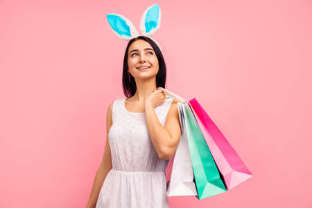 Beautiful woman in rabbit ears with shopping bags in her hands, spring shopping, a traditional holiday, in the studio on a pink background, Easter moodの写真素材