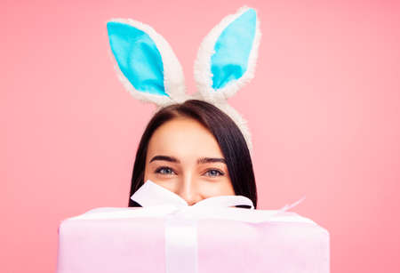 Happy woman in rabbit ears with a gift in her hands, a traditional holiday, in the studio on a pink...