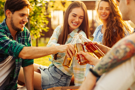 Young people have a picnic in nature. Young friends relax and eat pizza and drink drinks. A group of young people communicate while sitting on the grass in a summer park at sunset. Friends relax in their free time.の写真素材
