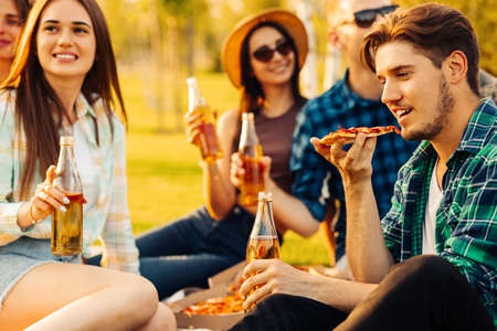group of friends are enjoying pizza in the park. Men and women sit on the grass around a pizza box. The concept of a picnic in the park, friends together in natureの写真素材
