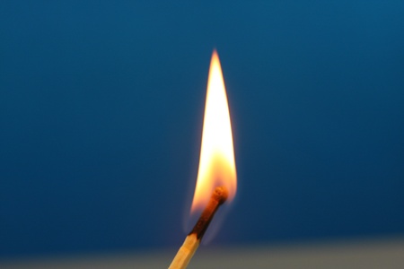Match burning with a yellow flame on a dark blue