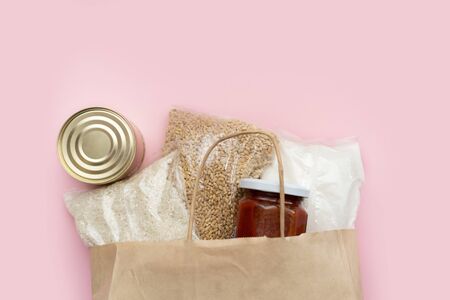 Food supply crisis food stock quarantine period isolation on a pink background. Rice, canned food, barley, tomato paste, sugar. Food Delivery, Donation, Coronavirus Quarantine. In a paper bagの写真素材