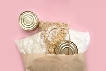 Food supply crisis food stock quarantine period isolation on a pink background. Rice, canned food, barley, sugar. Food Delivery, Donation, Coronavirus Quarantine. In a paper bagの写真素材
