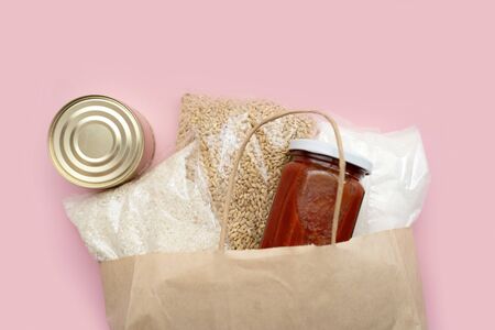 Food supply crisis food stock quarantine period isolation on a pink background. Rice, canned food, barley, tomato paste, sugar. Food Delivery, Donation, Coronavirus Quarantine. In a paper bagの写真素材