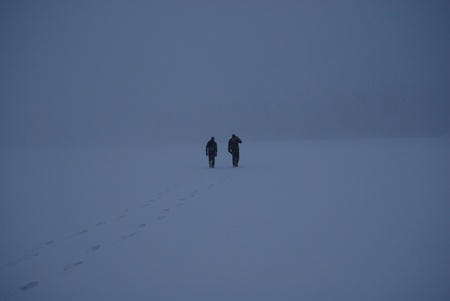 Two people walking on frozen foggy lakeの写真素材