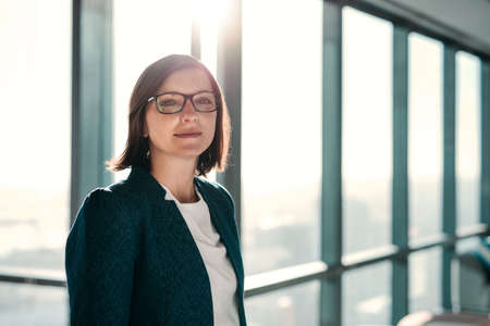 Portrait of an attractive businesswoman standing in front of windows in an office building overlooking the cityの写真素材