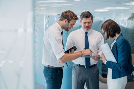Group of successful businesspeople talking together over paperwork while standing in an office